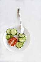 Sliced cucumber on a white plate and tomatoes photo