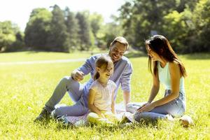 Familia joven feliz con linda hijita divirtiéndose en el parque en un día soleado foto