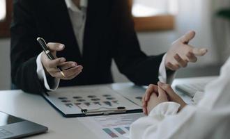 Team businesswoman explaining the structure of the business and another employee listens discreetly. along with the documents on the desk and laptop in the office photo