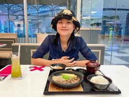 Happy young Asian woman smiling and enjoying eating Japanese food in a restaurant during coronavirus or covid-19 outbreak. photo