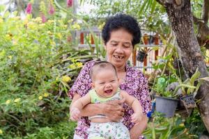 Happy big laughing child boy and senior woman holding adorable baby boy in flowery garden. photo