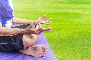 Closeup of aged woman hands meditating in lotus position on yoga mat at green grass background. photo