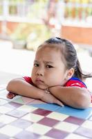 Angry little girl sitting and looking at camera. Unhappy child feeling upset and sad with a negative attitude. photo