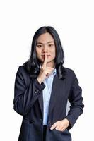 Portrait of young businesswoman holding a finger on her lips - silent gesture. Happy female saying 'shh', asking to keep silent about her secret on white background. photo