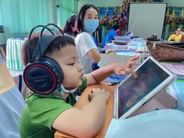 Suphan Buri, Thailand, February 10, 2021 -Preschooler boy watching cartoon movie from tablet while waiting for his mother meeting room