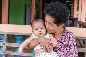 Happy senior woman holding adorable baby boy on lap at home. photo