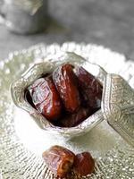 High angle view of medjool dates in small silver Turkish bowl on silver plate with blur background photo