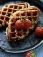 Close up view of Croffle, modern take out or delivery food, served with strawberries on the vintage plate and blue table. photo