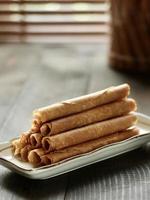 High angle view of Indonesian crispy egg roll called semprong cake on wooden cutting board with blurred bamboo window at the back. photo