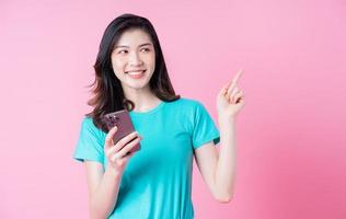 Joven mujer asiática con smartphone sobre fondo rosa