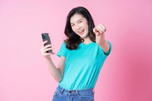 Young Asian woman using smartphone on pink background photo