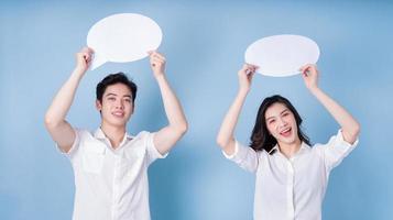 Image of young Asian couple holding message bubble on blue background photo