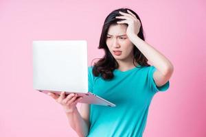 Young Asian woman using laptop on pink background photo