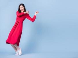 Full length image of young Asian woman wearing red dress on blue background photo