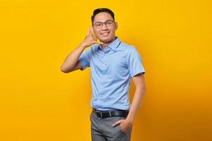 smiling young asian man in glasses  showing call me hand gesture isolated on yellow background. businessman and entrepreneur concept photo