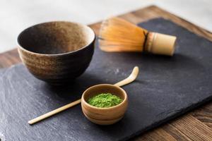 Té matcha verde prepearing sobre mesa de piedra negra foto