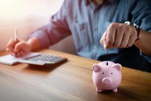 image of man hand putting coins in pink piggy bank for account save money. Planning step up, saving money for future plan, retirement fund. Business investment-finance accounting concept. photo
