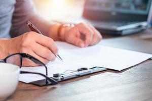 Close-up of Hand using writing pen with questionnaire or paperwork survey question filling in business company personal information form checklist document. photo