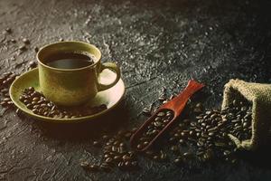 Hot black coffee in vintage brown ceramic cup with coffee beans roasted in burlap sack bag on dark grunge rustic table background. Flat lay with copy space. photo