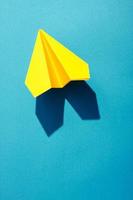 Yellow paper jet on blue background under the bright light. photo