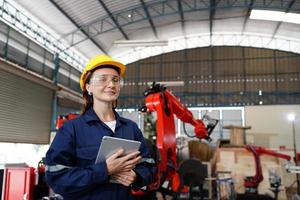 Professional young industrial factory woman employee working with machine part, checking and testing industrial equipment and robot arms in large Electric electronics wire and manufacturing plant photo