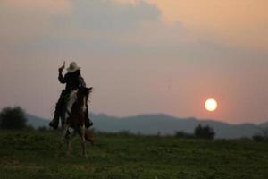 vaquero a caballo contra una hermosa puesta de sol, vaquero y caballo a primera luz, montaña, río y estilo de vida con fondo de luz natural foto