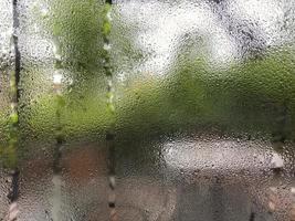 Wet window glass from steam condensation water drops after the rain foreground with blur terrace garden background. Selective focus.