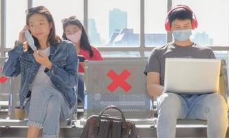 el grupo de viajeros asiáticos vive de nuevas formas normales para prevenir la infección por covid-19 en el área pública. mujer joven con mascarilla protectora y sentada distanciándose entre sí. enfoque selectivo.