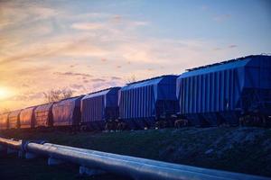 tren con vagones cargados de granos se mueve al atardecer a lo largo del oleoducto.