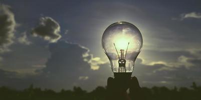 sostenga a mano una bombilla con el concepto de energía solar con fondo de cielo foto