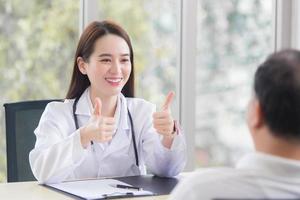 Asian professional woman doctor smiles and shows thump up sign or Very good with her patient due to his healthcare at hospital. photo