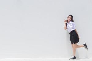 A beautiful Asian girl in a cheerful school uniform is smiling and showing her finger to present some product with a white background. photo