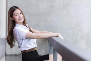 Portrait of an adult Thai student girl in university student uniform. Asian beautiful girl sitting smiling happily at university photo