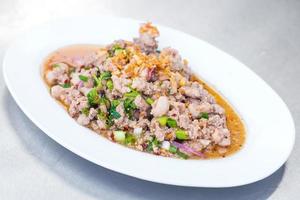Spicy minced pork salad is traditional food of Northeast of Thailand. It contains minced pork, roasted rice, roasted chili and Thai herbs mixed together. It was put on white plate. photo