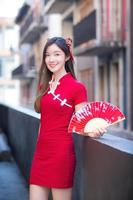 hermosa mujer asiática vestida de rojo se encuentra sosteniendo un abanico entre el tema del año nuevo chino en el centro de la ciudad vieja. foto