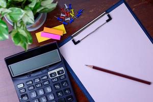 Calculator, file, pencil and office supplies. Placed beside a tree on a wooden table. photo