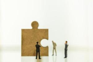 Business, Teamwork, Planning and Work Concept. Close up of group of businessman miniature figure people standing and looking to wooden jigsaw piece with copy space. photo