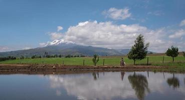 Beautiful Hispanic woman walks with a dress and hat on a dirt road with the Cayambe volcano in the background during a sunny morning and blue sky photo