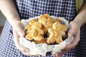 manos de mujer sosteniendo galletas navideñas caseras, galletas de nuez de cajú recién horneadas en forma de muñeca en una mesa blanca foto