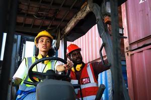 Industrial workers wear safety vest and helmet driving forklift car at plant factory industry, two African American engineer man and woman work together at logistic shipping cargo container yard.