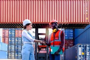 Two worker wearing safety helmet shaking hands at logistic shipping cargo containers yard. African American engineer man having hand shack with his beautiful young woman boss after work discussion photo