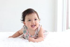 Portrait of a six months crawling baby on fluffy white rug, happy smiling adorable sweet little girl kid lying on bed in bedroom, childhood and baby care concept photo