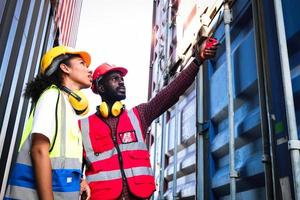 Two industrial African American engineer man and woman wearing safety vest and helmet working together at logistic shipping cargo container yard, worker man holding walkie-talkie and pointing away. photo