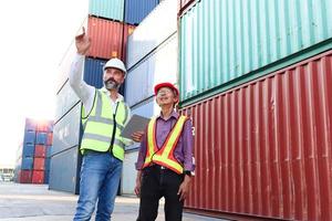 dos trabajadores con chaleco de seguridad y casco discutiendo en el patio de contenedores de carga de envío logístico. Ingeniero trabajador asiático mayor serio hablando con su jefe en el lugar de trabajo.