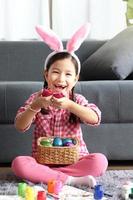 Happy adorable pink little Easter bunny girl kid with rabbit ears headband smiling and laughing after finding colorful Easter egg, egg hunt game, celebration of spring beginning. photo