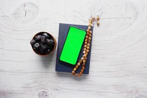 smart phone, Holy book Quran and rosary on table, photo