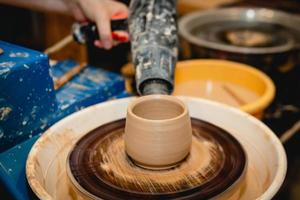 Potter working on potters wheel with clay. Process of making ceramic tableware in pottery workshop. photo