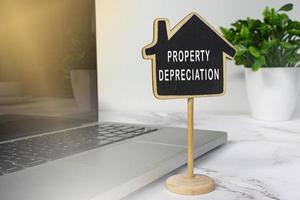 Property depreciation text on wooden house model with notebook on white desk. photo