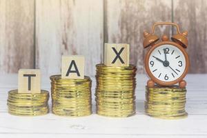 Tax text on wooden blocks and alarm clock set at 10 o'clock with gold coins. photo