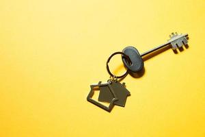 Key chain in the shape of wooden house with key on a yellow background. Building, design, project, moving to new home, mortgage, rent and purchase real estate. Copy space photo